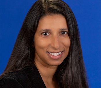 Woman in dark clothing with long, brown hair smiling into camera.